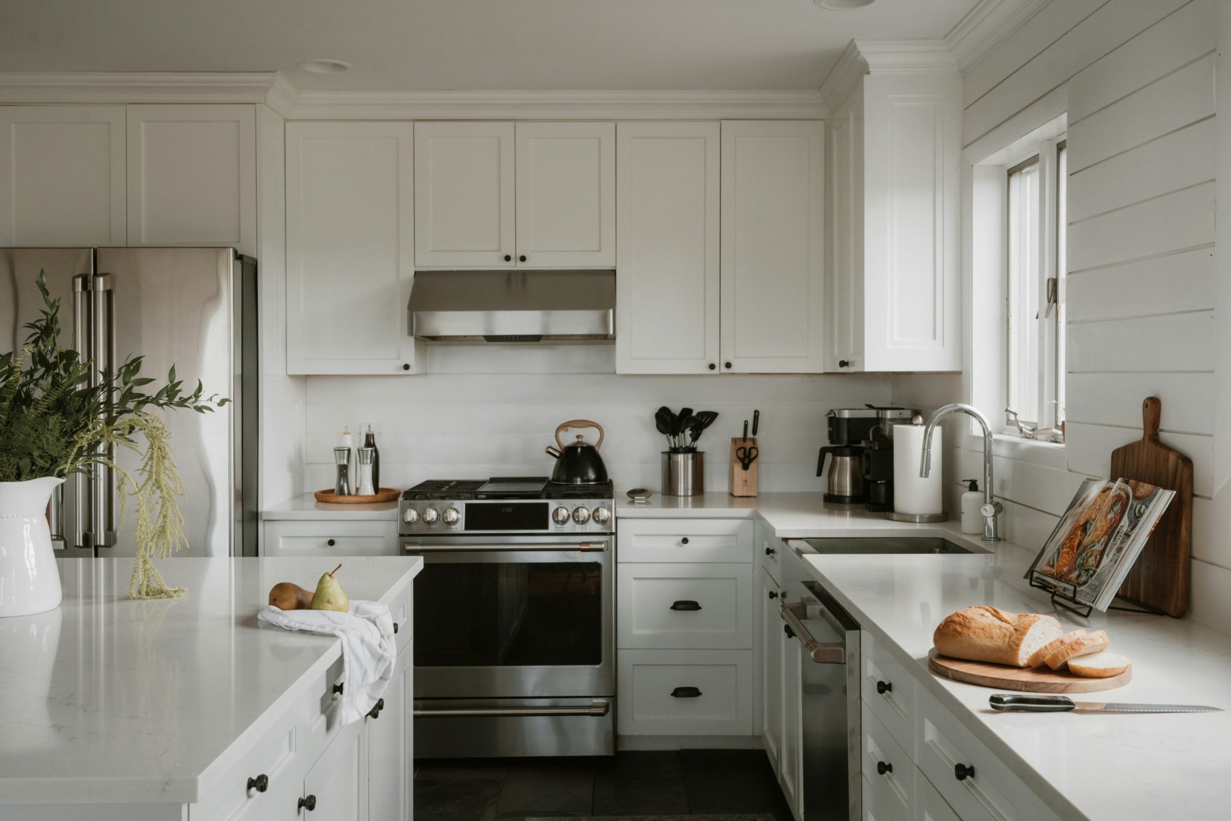 Bright white kitchen with stainless range, quartz counters and fresh bread